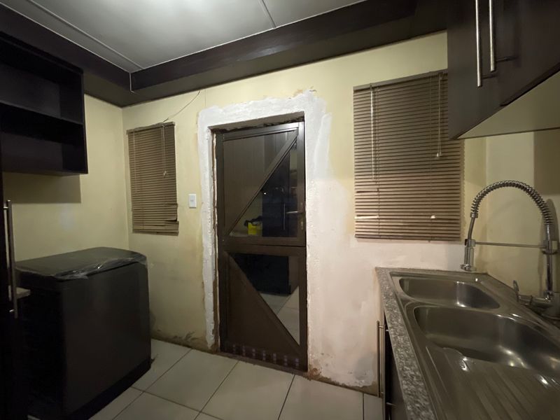 A functional scullery area featuring a double sink, built-in cabinetry, and tiled flooring, currently requiring cosmetic wall repairs and finishing touches.