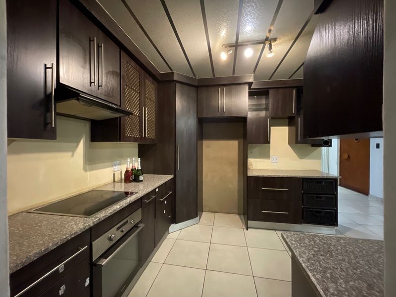 Modern kitchen featuring dark wood cabinetry, granite countertops, built-in oven, electric hob, and tiled flooring with integrated lighting.