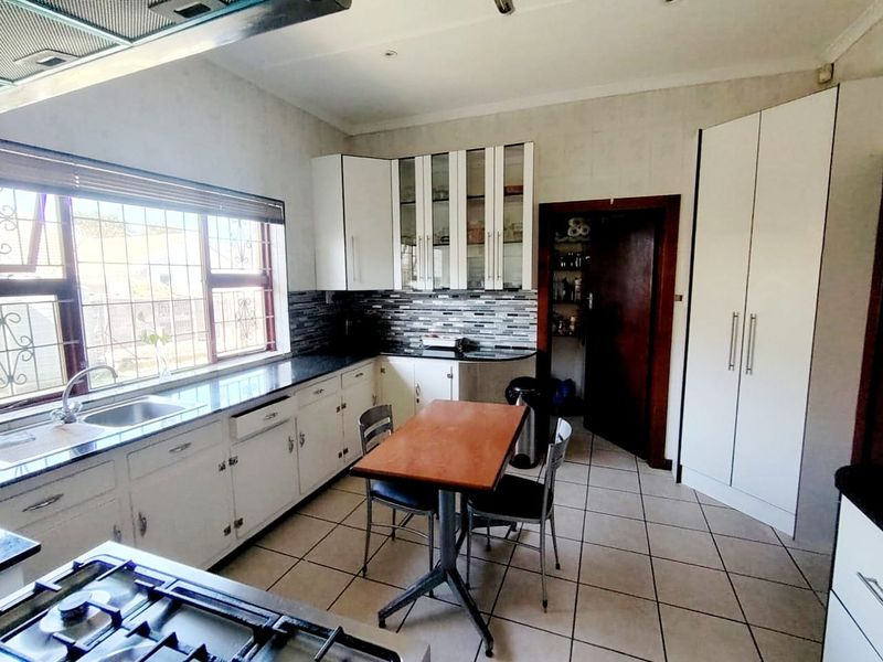 Functional kitchen featuring white cabinetry, granite countertops, gas hob, extractor fan, and tiled flooring with an adjacent pantry.