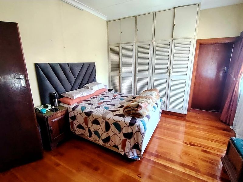 A bedroom featuring polished hardwood flooring and extensive built-in louvered cupboards, offering ample storage space.