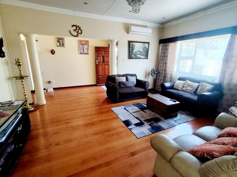 Spacious living room featuring warm laminate flooring, decorative columns, recessed lighting, and a wall-mounted air conditioning unit.