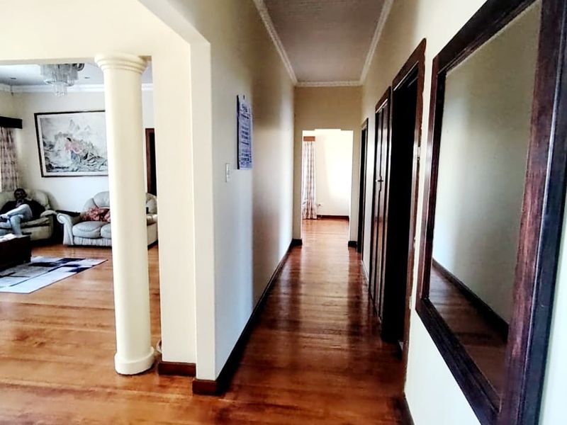 A spacious hallway featuring polished hardwood flooring, crown molding, and a decorative column leading into the adjacent living area.
