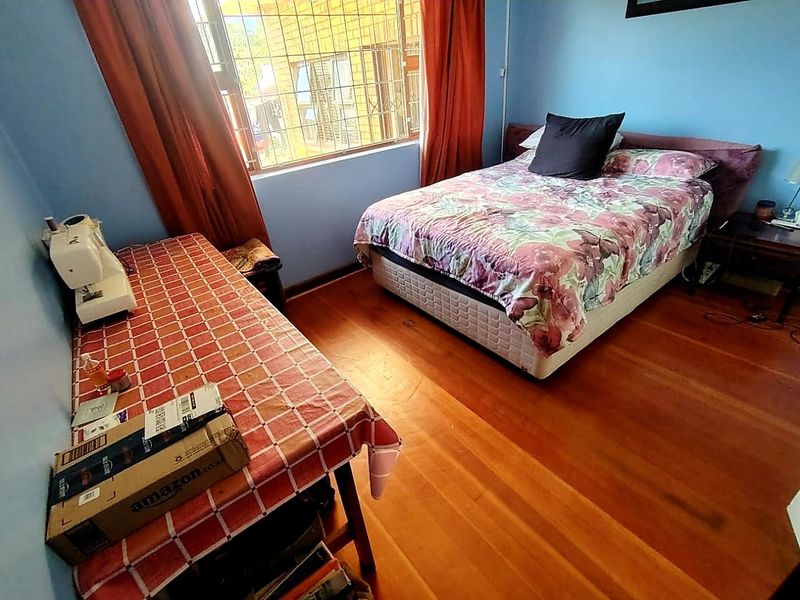 A bedroom featuring timber flooring and a window fitted with security bars, providing natural light to the space.