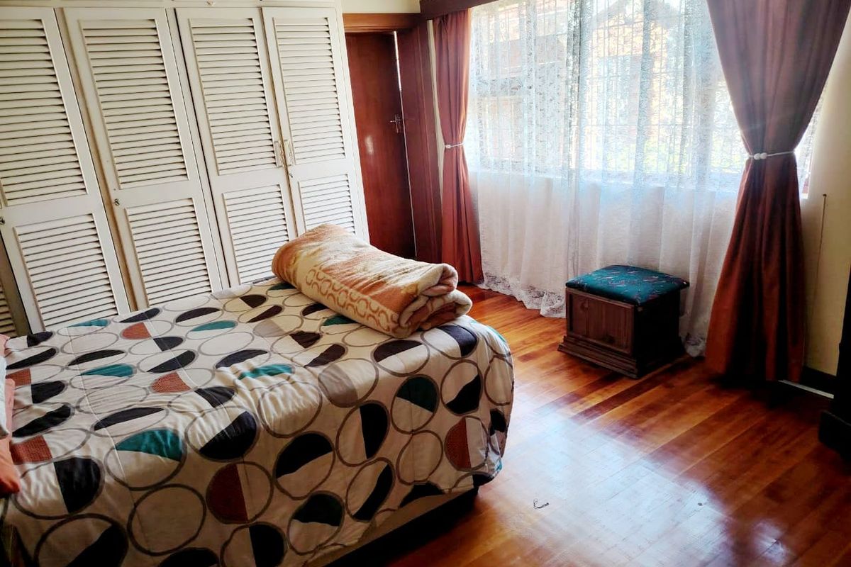 A bedroom featuring polished hardwood flooring, extensive built-in cupboard storage, and a large window with security bars.