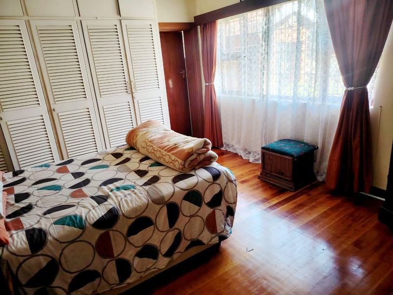 A bedroom featuring polished hardwood flooring, extensive built-in cupboard storage, and a large window with security bars.