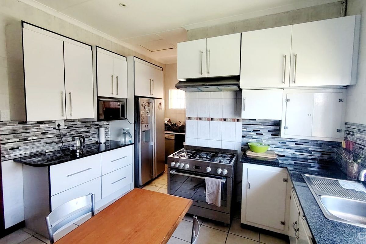 A functional kitchen featuring white cabinetry, granite countertops, a gas stove with extractor fan, and a modern tiled backsplash.