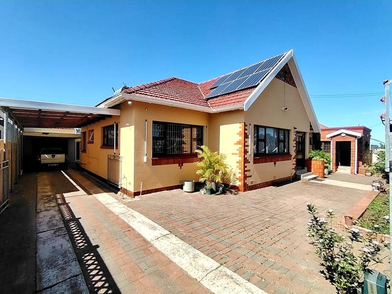 Front exterior view of a single-story house featuring a tiled roof, solar panels, a paved driveway, and a covered carport area.