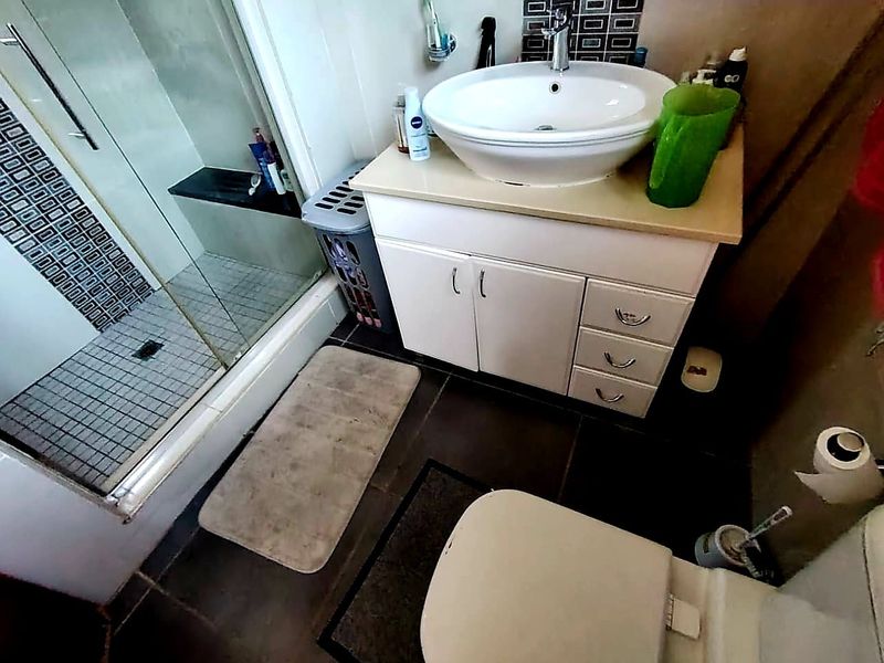 Compact bathroom featuring a vanity with vessel sink, glass-enclosed shower, and tiled flooring.
