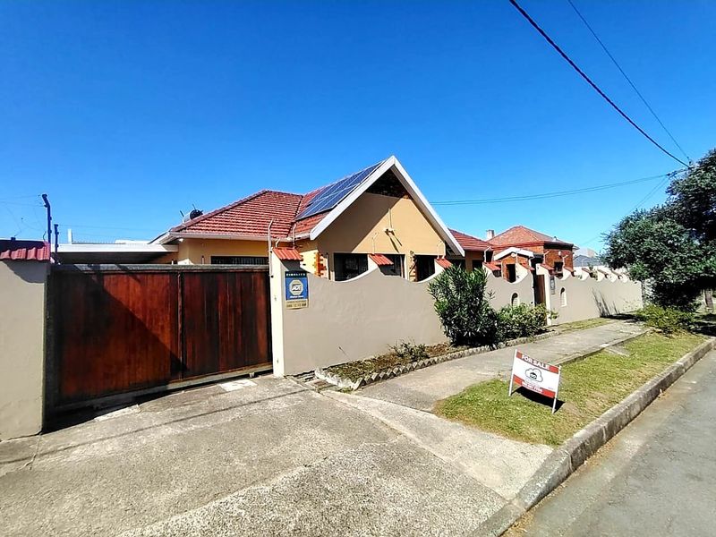 Front exterior view of a residential house featuring a tiled roof, solar panels, and a secure perimeter wall with a sliding gate.