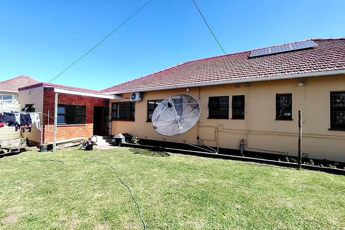 Rear view of the house featuring a tiled roof with solar panels, brick and plastered exterior walls, and security bars on the windows.