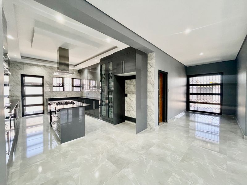 Modern, spacious kitchen featuring high-gloss cabinetry, a central island with a gas hob, marble-look floor tiles, and recessed ceiling lighting.