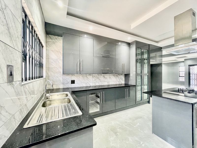 Modern kitchen featuring high-gloss grey cabinetry, granite countertops, marble-look wall tiles, and integrated stainless steel appliances in a clean, contemporary finish.