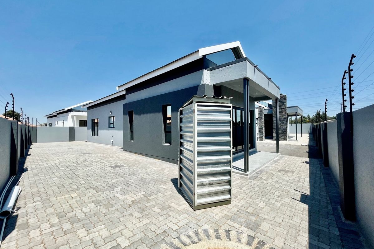 Rear view of a modern house featuring a paved driveway, covered patio, and secure boundary walls with electric fencing.