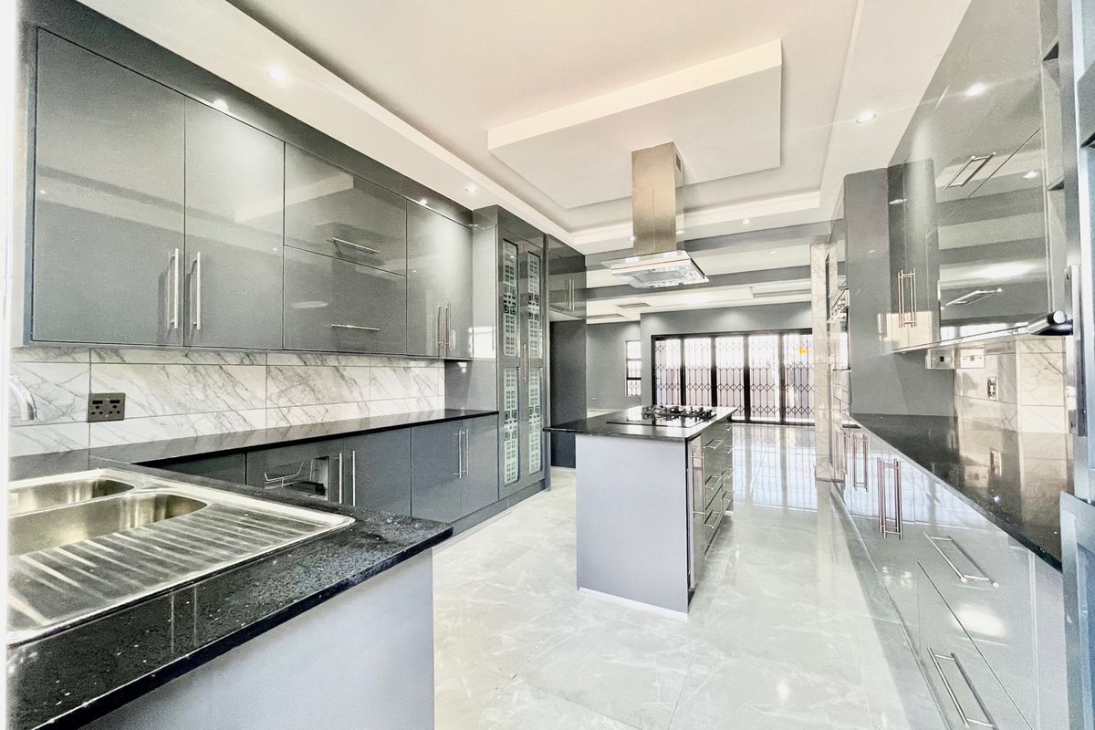 Modern, spacious kitchen featuring high-gloss cabinetry, granite countertops, a central island with a built-in hob, and elegant marble-look backsplash tiling.
