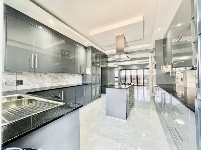 Modern, spacious kitchen featuring high-gloss cabinetry, granite countertops, a central island with a built-in hob, and elegant marble-look backsplash tiling.