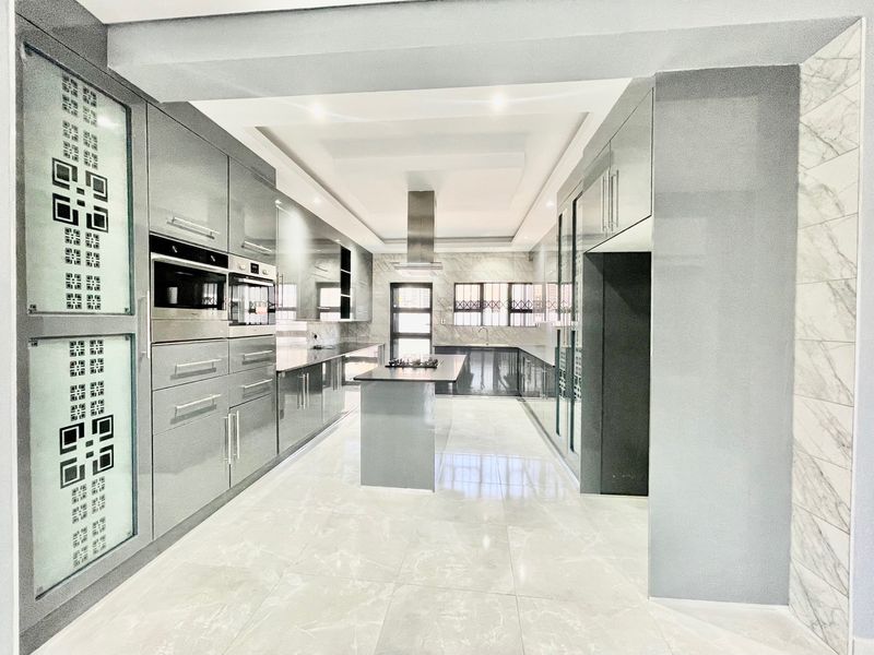 Modern, high-end kitchen featuring sleek grey cabinetry, a central island with a built-in hob, integrated appliances, and polished marble-look floor tiles.