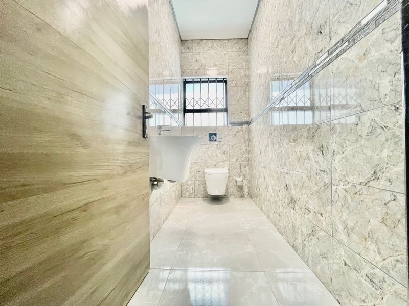 A modern, minimalist bathroom featuring floor-to-ceiling marble-effect tiling, a wall-mounted basin, and a wall-mounted toilet with security bars on the window.
