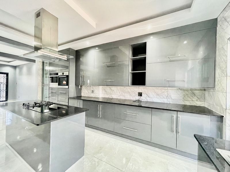 Modern kitchen featuring high-gloss cabinetry, granite countertops, a central island with a gas hob, and integrated built-in appliances.