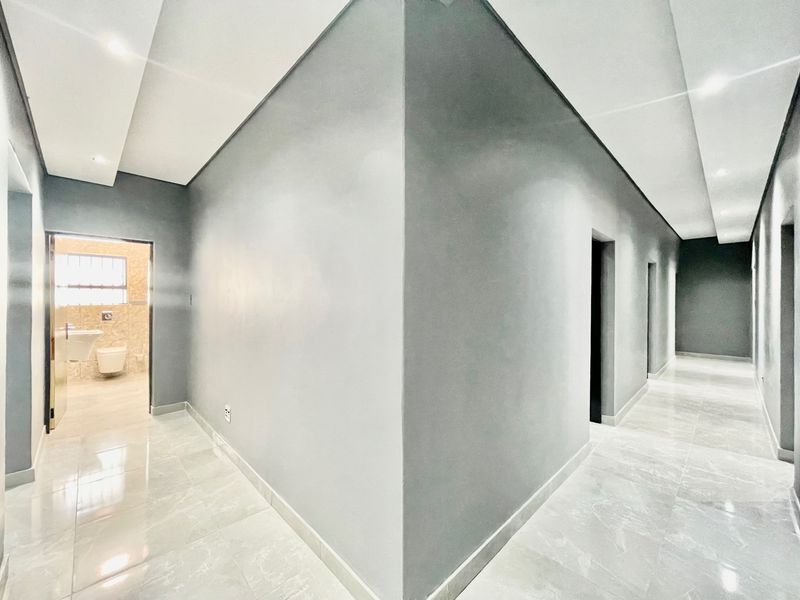 A modern, spacious hallway featuring neutral grey walls, polished tiled flooring, and recessed ceiling lighting, leading to multiple rooms including a bathroom.