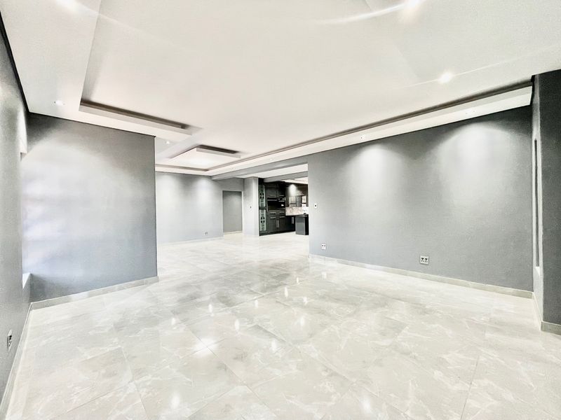 Spacious open-plan living area featuring modern recessed ceilings, downlighting, and polished marble-look floor tiles, leading into a contemporary kitchen space.