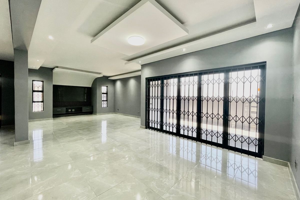 Spacious, modern living area featuring polished porcelain tiles, recessed ceiling lighting, and large sliding doors with security gates leading to the exterior.