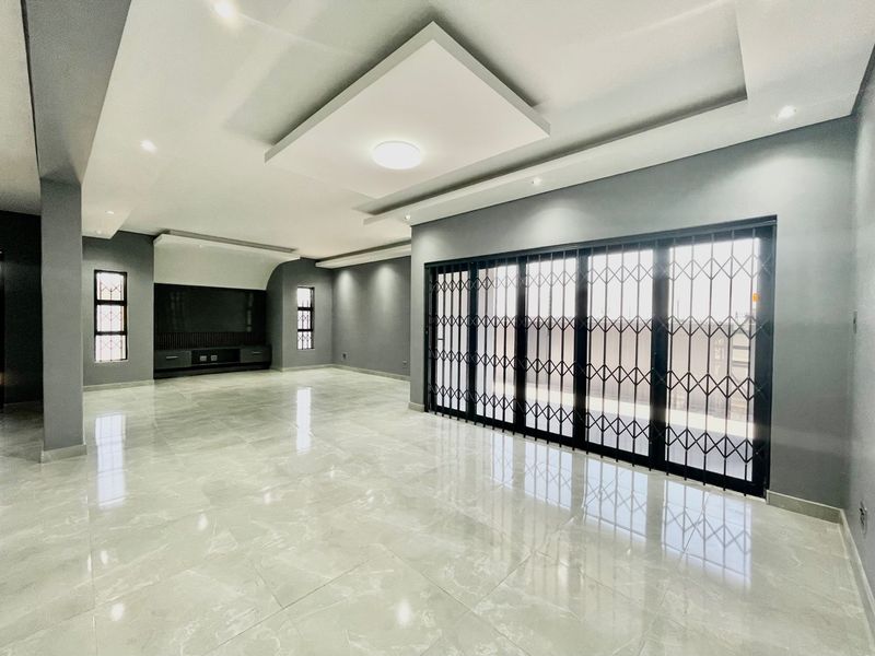 Spacious, modern living area featuring polished porcelain tiles, recessed ceiling lighting, and large sliding doors with security gates leading to the exterior.