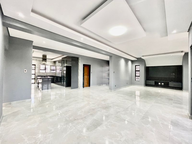 Spacious open-plan living area featuring modern porcelain tiling, a recessed ceiling with integrated lighting, and a sleek, contemporary kitchen with built-in cabinetry.