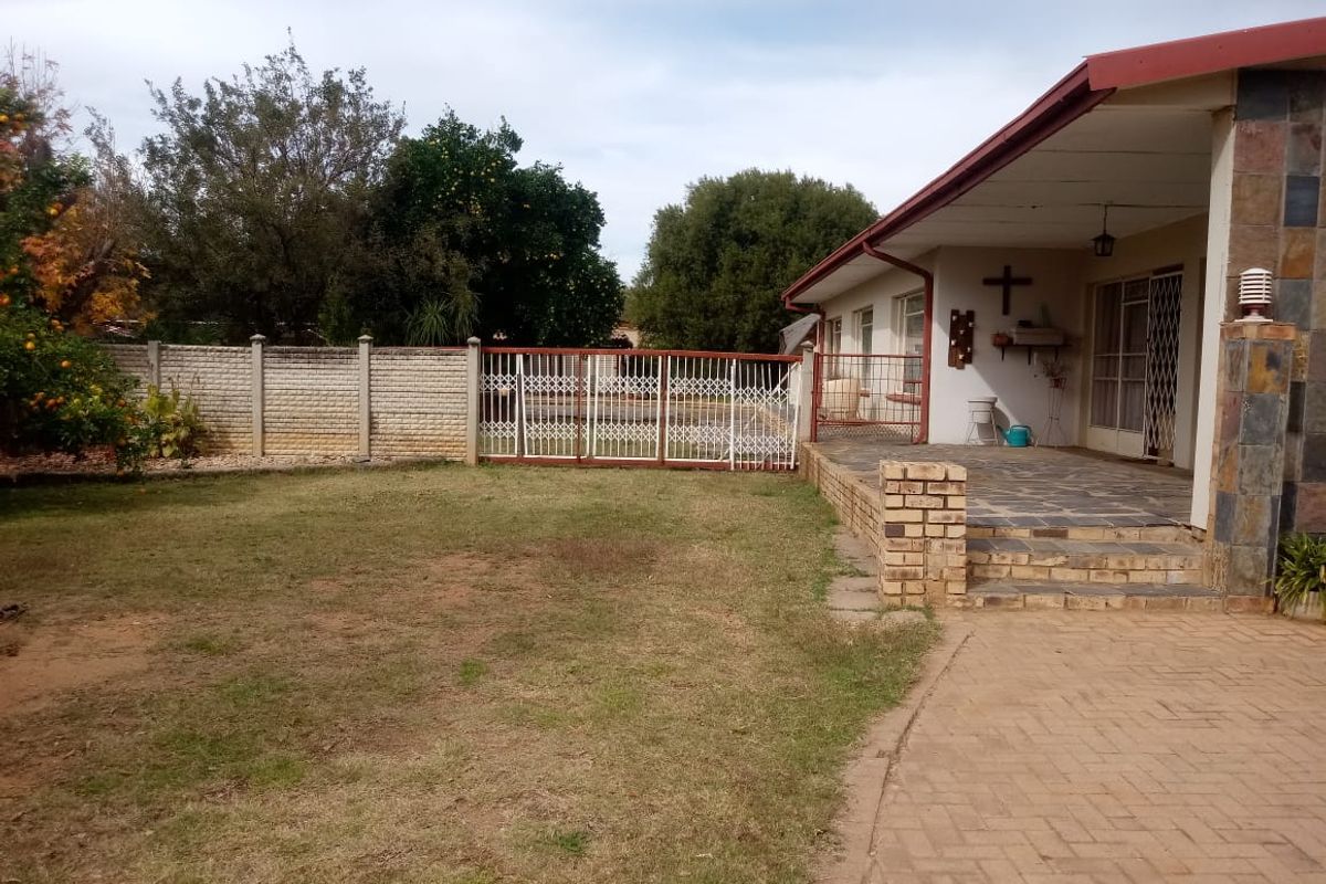 Rear view of the property featuring a covered patio with stone cladding, brick paving, and a spacious garden area enclosed by a boundary wall.