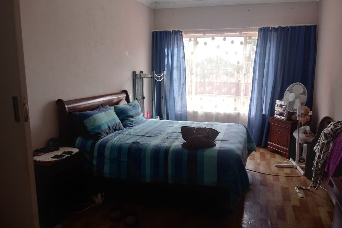 A standard bedroom featuring laminate flooring, a large window with natural light, and coved ceiling detailing.