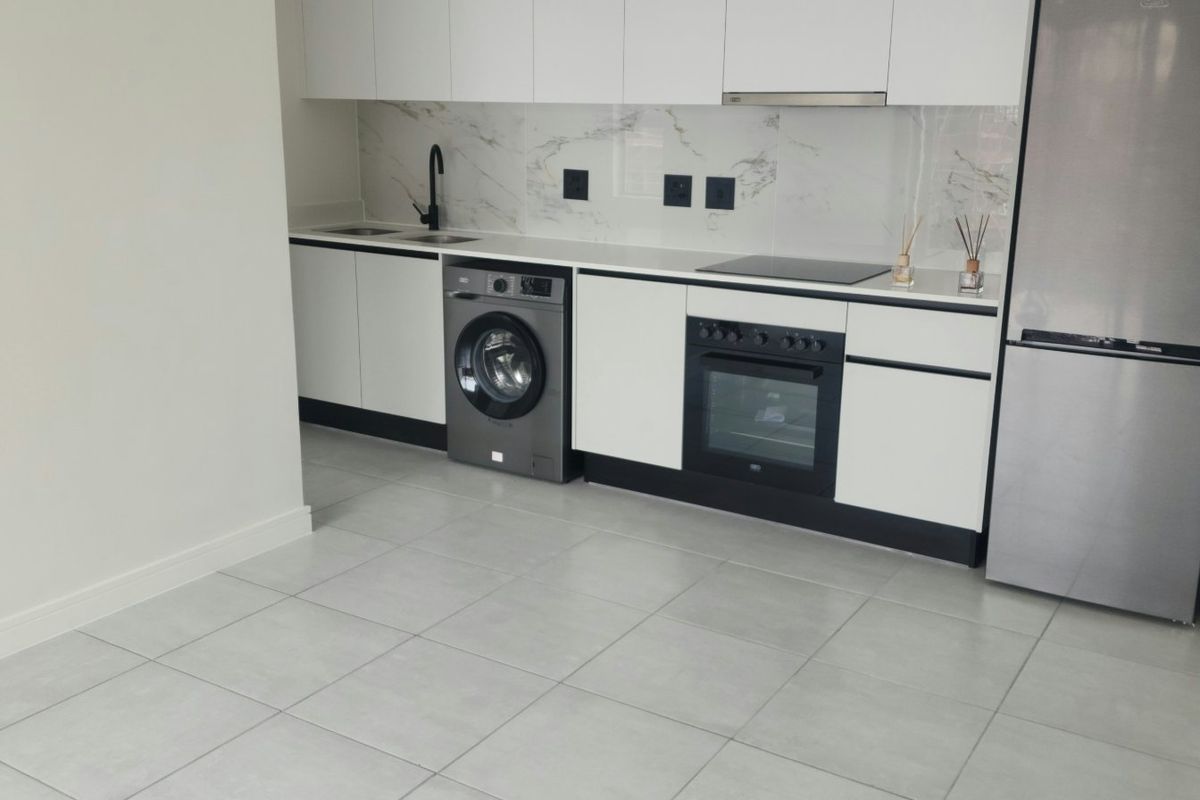 Modern kitchen featuring sleek white cabinetry, marble-look splashback, integrated oven and hob, and contemporary tiled flooring in an open-plan layout.