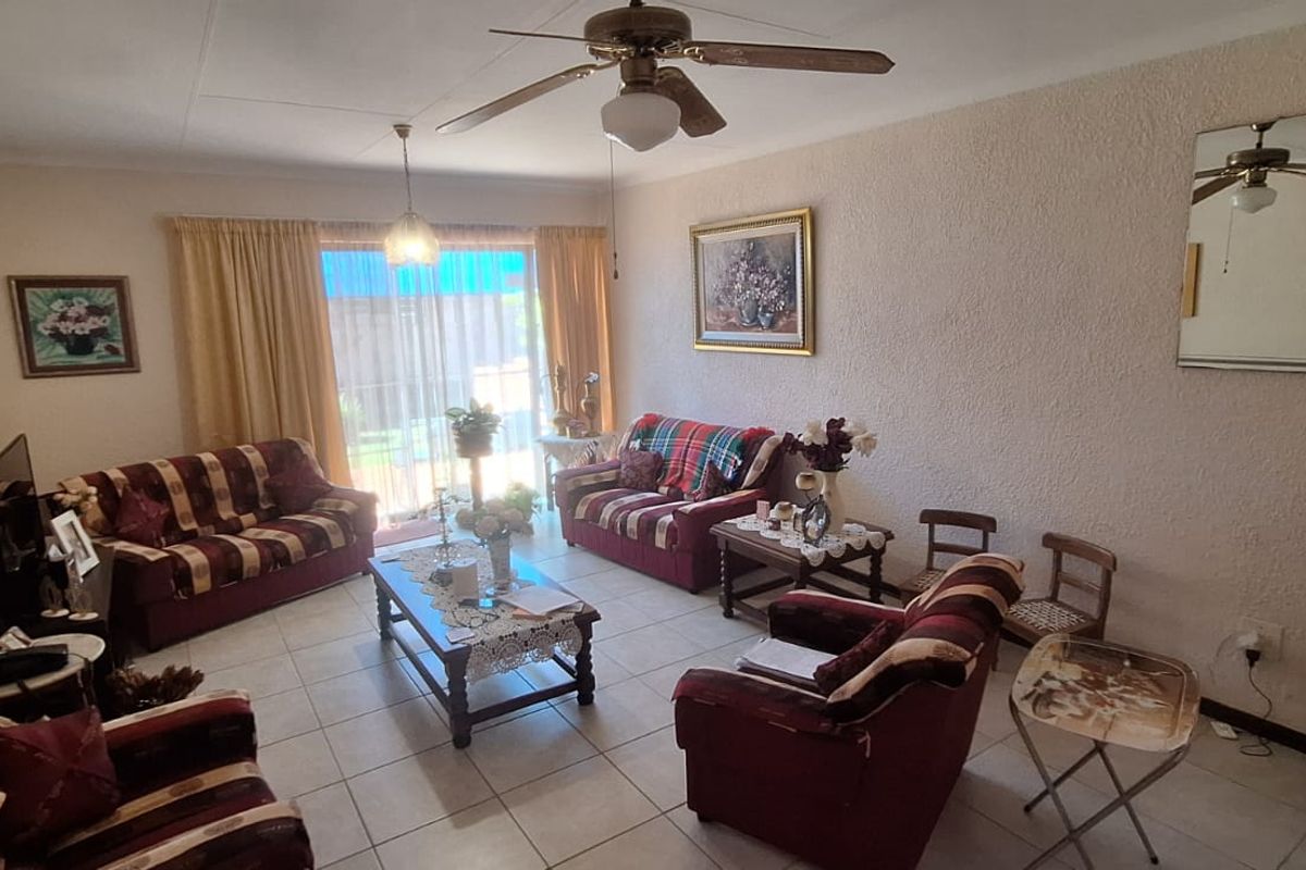 A spacious living room featuring tiled flooring, a ceiling fan, and a sliding glass door providing access to the outdoor area.