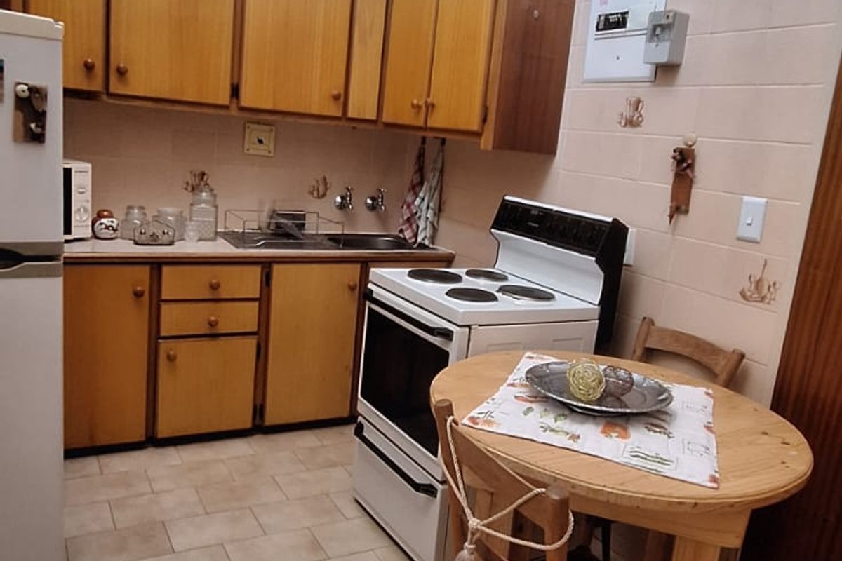 A dated kitchen featuring wooden cabinetry, a tiled splashback, a double sink, a freestanding stove, and a large skylight providing natural light.
