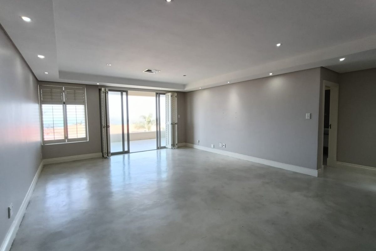 Spacious, light-filled living area featuring polished concrete floors, recessed downlighting, and bi-fold doors opening onto an outdoor balcony.