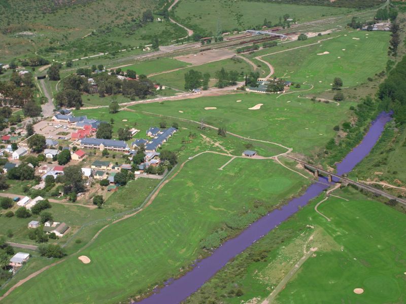 An aerial view of a residential area adjacent to a golf course, river, and railway infrastructure.