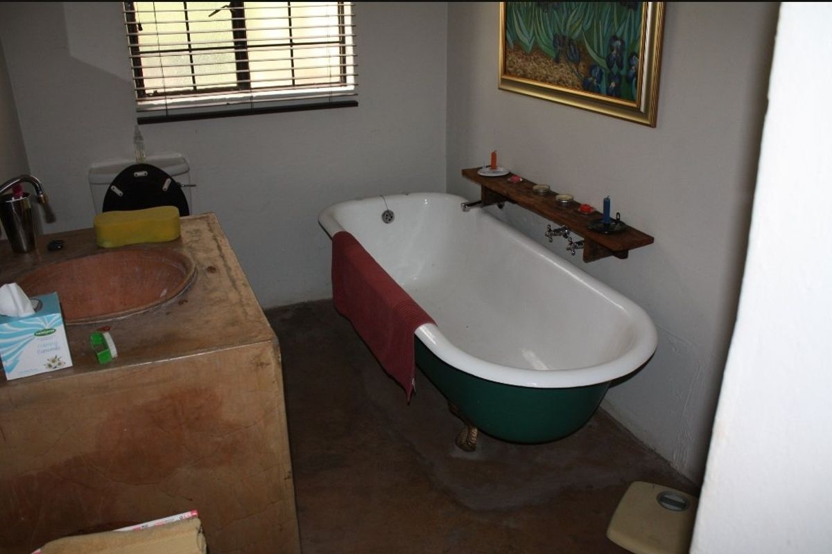 A rustic bathroom featuring a vintage clawfoot bathtub, a custom concrete vanity with basin, and a toilet, requiring cosmetic updates to finishes.