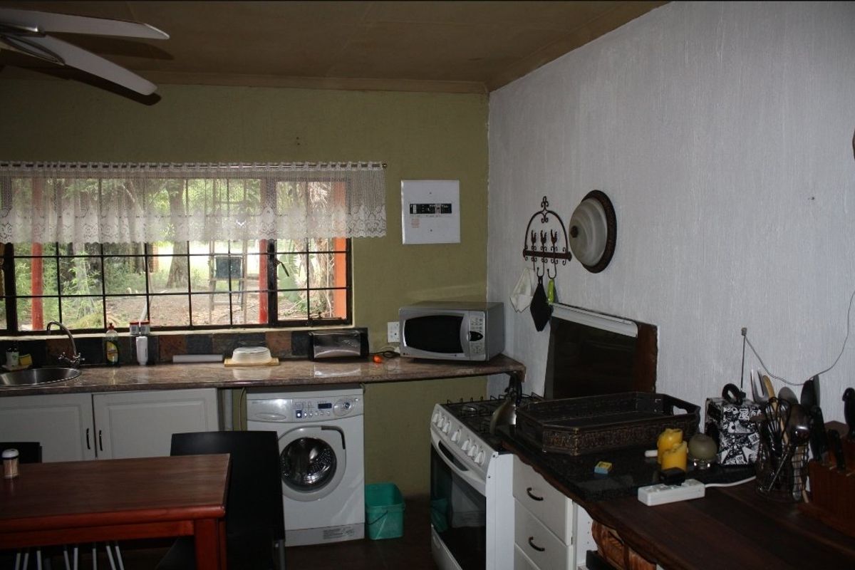 A functional kitchen area featuring built-in cabinetry, a stainless steel sink, a freestanding stove, and an integrated washing machine with garden views.