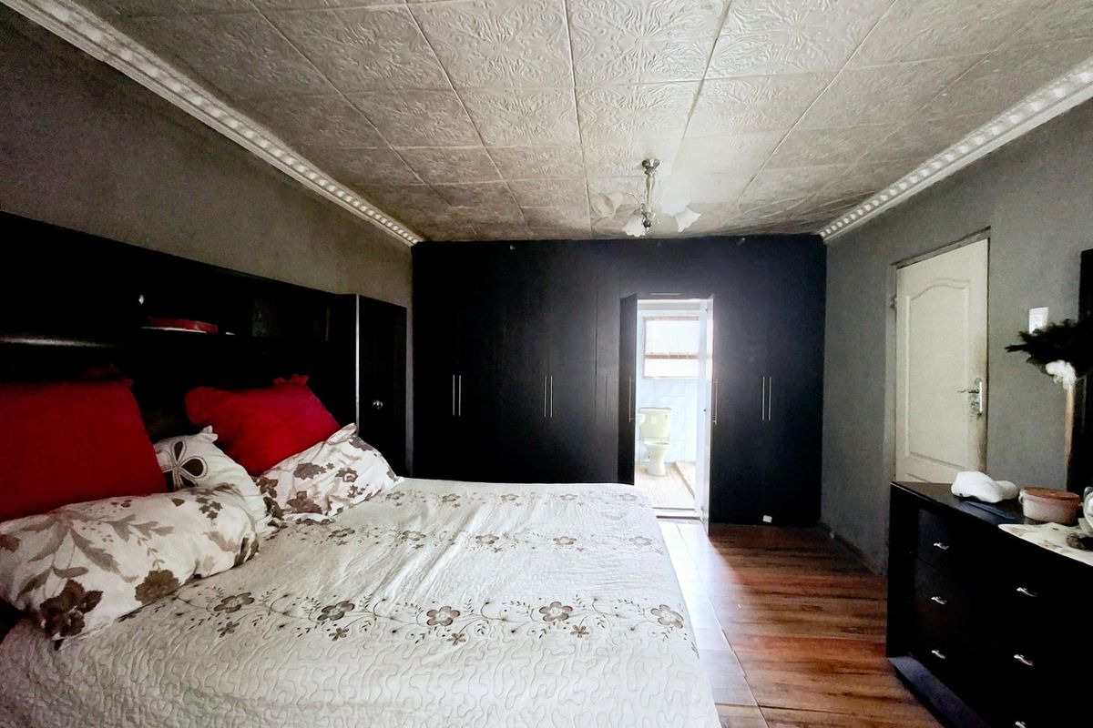 Spacious bedroom featuring built-in cupboards, a decorative pressed metal ceiling with coving, and tiled flooring, with direct access to an en-suite bathroom.