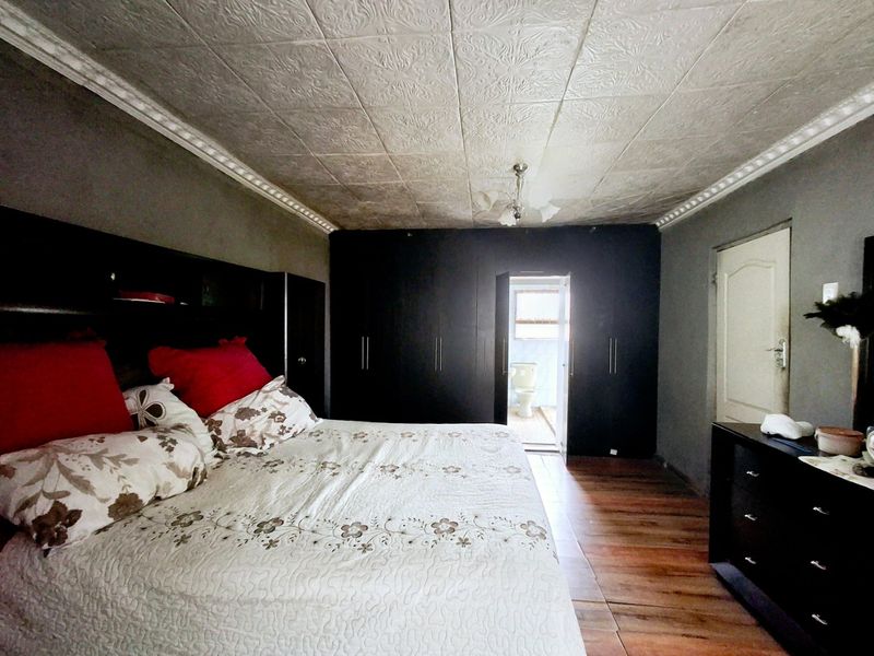 Spacious bedroom featuring built-in cupboards, a decorative pressed metal ceiling with coving, and tiled flooring, with direct access to an en-suite bathroom.