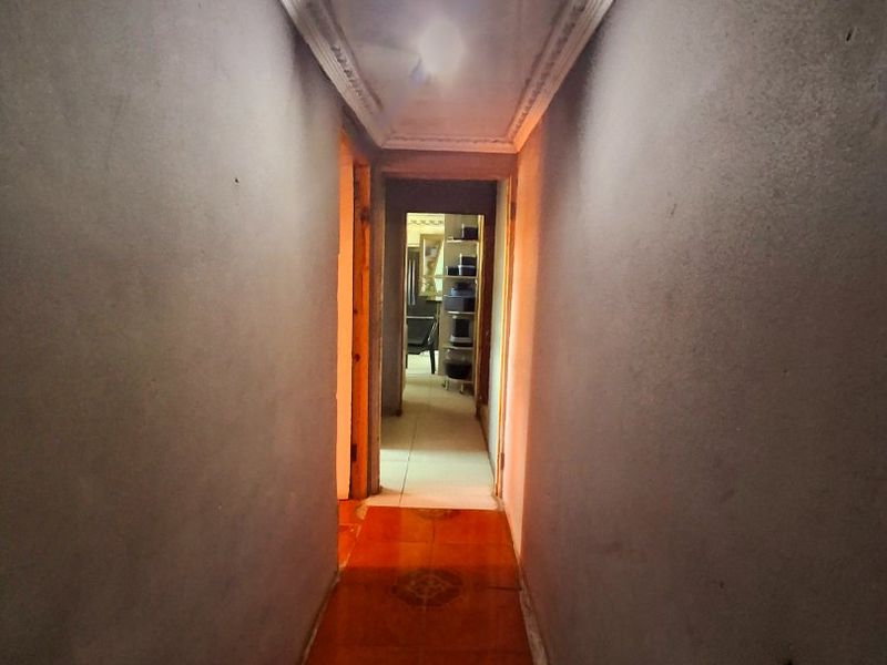 A narrow interior hallway featuring decorative ceiling cornicing and tiled flooring, leading towards an adjacent room.