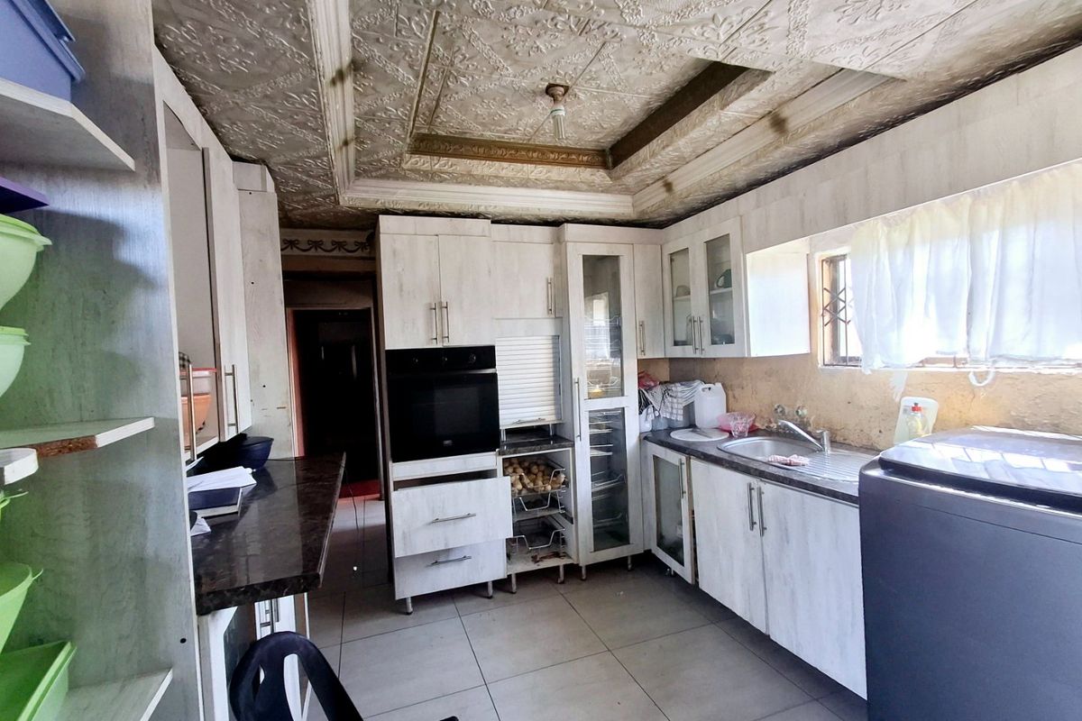 A functional kitchen featuring built-in cabinetry, an integrated oven, and a stainless steel sink, with decorative ceiling tiles and tiled flooring throughout.