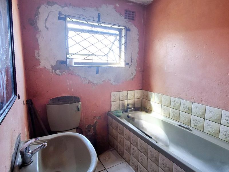 A dated bathroom requiring significant renovation, featuring a pedestal basin, bathtub, and toilet, with visible wall damage and worn finishes throughout.