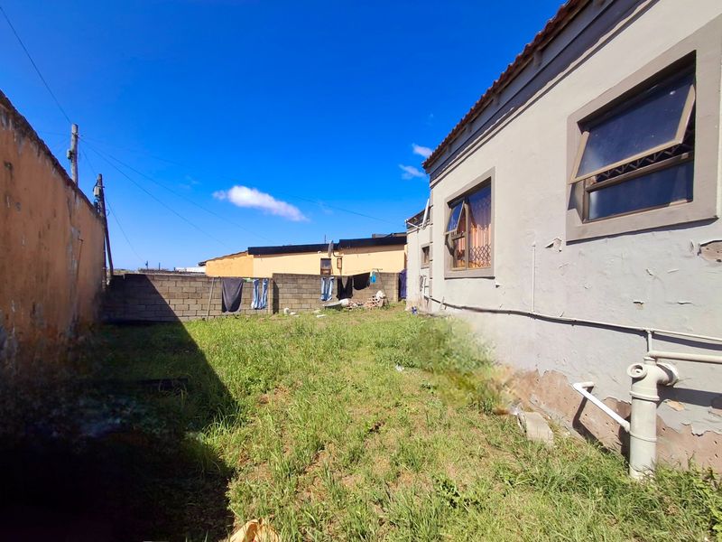 Rear exterior view of the property showing a grassed yard, boundary walls, and the side elevation of the house with visible paint deterioration.