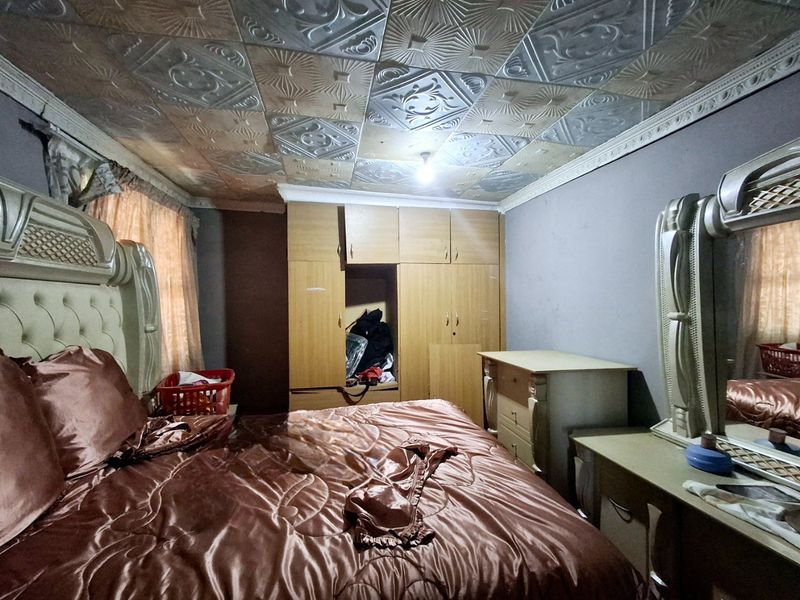 A bedroom featuring built-in wooden wardrobes and decorative ceiling tiles, requiring some maintenance and cosmetic updates to improve the overall aesthetic.