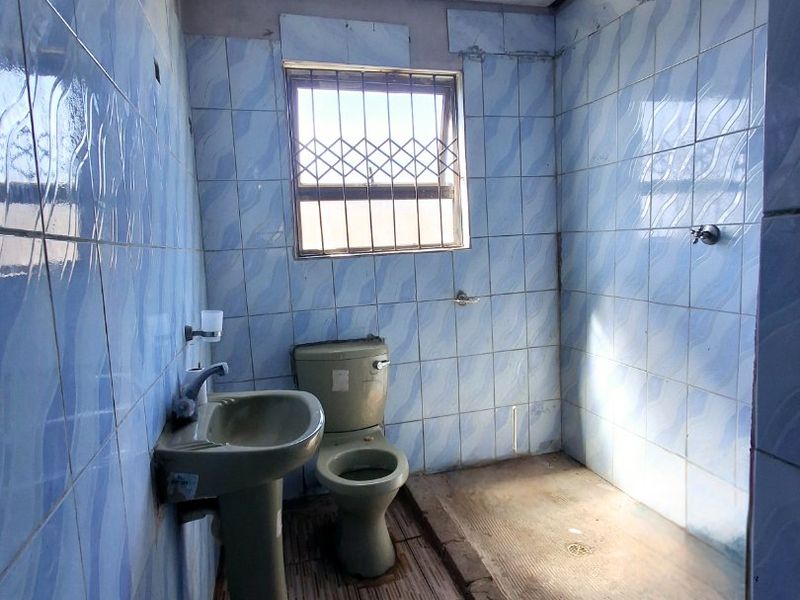 A dated bathroom featuring a pedestal basin, toilet, and open shower area with blue wall tiles and tiled flooring.