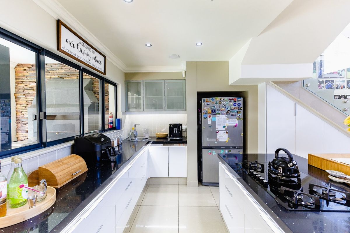 Modern kitchen featuring sleek white cabinetry, black granite countertops, a built-in gas hob, and tiled flooring with integrated lighting.