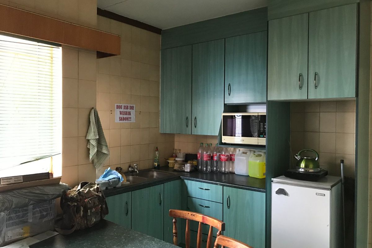 A dated kitchen featuring green laminate cabinetry, tiled backsplash, and a stainless steel sink, offering potential for a modern renovation.