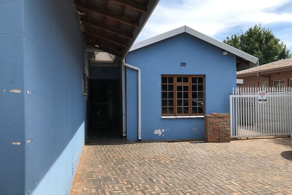 Rear exterior view of the commercial property featuring a paved courtyard, blue painted walls, and a security gate.