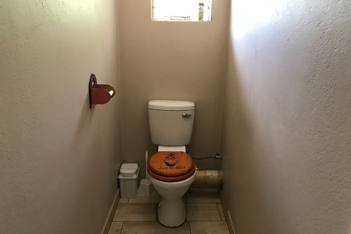 A compact guest bathroom featuring tiled flooring and a standard toilet, requiring minor cosmetic updates to conceal exposed plumbing.