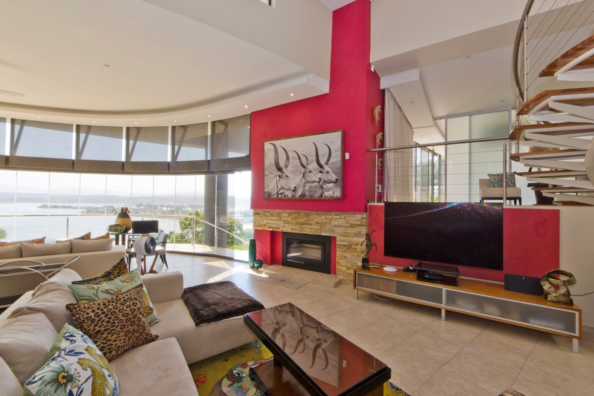 Spacious living room featuring a striking red accent wall, built-in fireplace with stone cladding, spiral staircase, and expansive floor-to-ceiling windows with panoramic views.