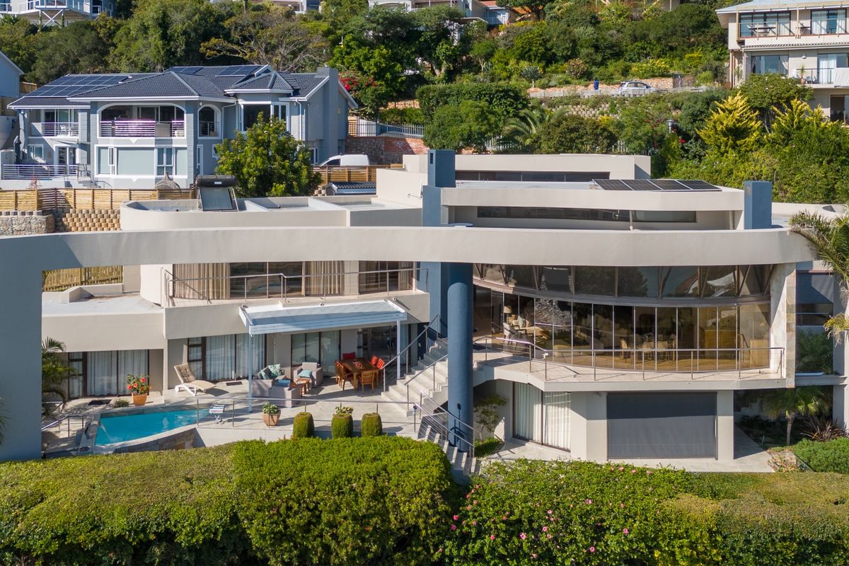 Aerial view of a modern multi-level residence featuring a swimming pool, expansive terraces, solar panels, and integrated garage in a hillside setting.